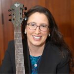 Cantor Bryce Megdal smiling holding her guitar